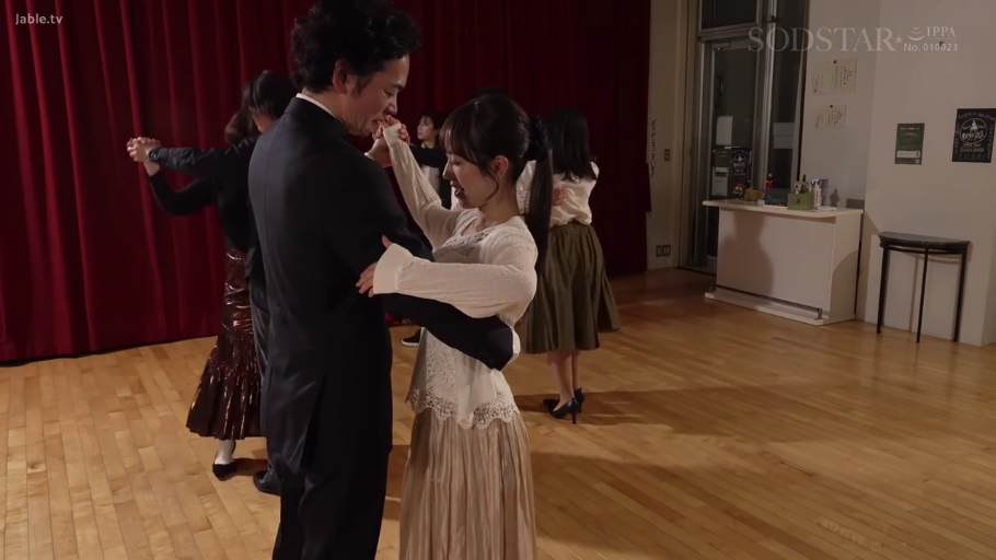 微笑 · 舞蹈教室 · 无 · 两人上半身特写 · 女人穿白色蕾丝长袖上衣和米色长裙 · 背景有红色幕布